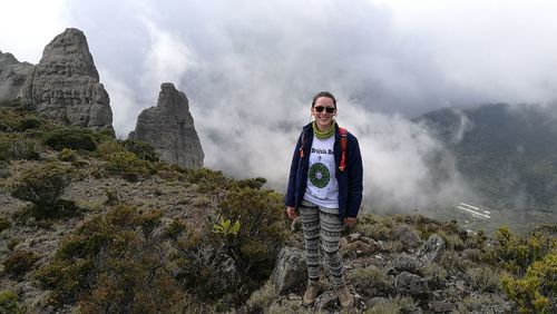 Portrait of young man standing on rock against sky