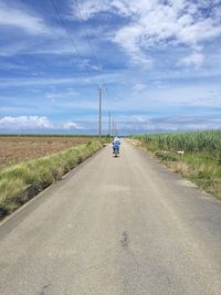 Rear view of man riding bicycle on road against blue sky