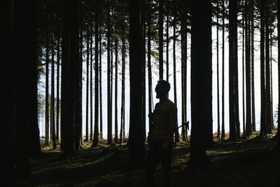 Rear view of silhouette man standing by trees in forest