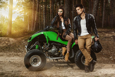 Full length of man and woman wearing leather jacket by quadbike in forest