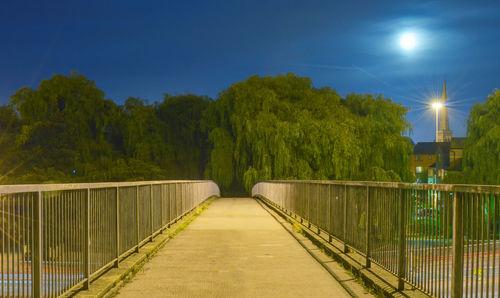 Footbridge amidst trees against sky at night