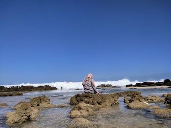 Rear view of woman standing at beach against clear blue sky