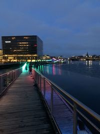 Illuminated bridge over river by buildings against sky at night