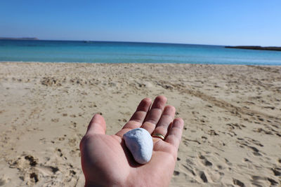 Close-up of hand on sand at beach against clear sky