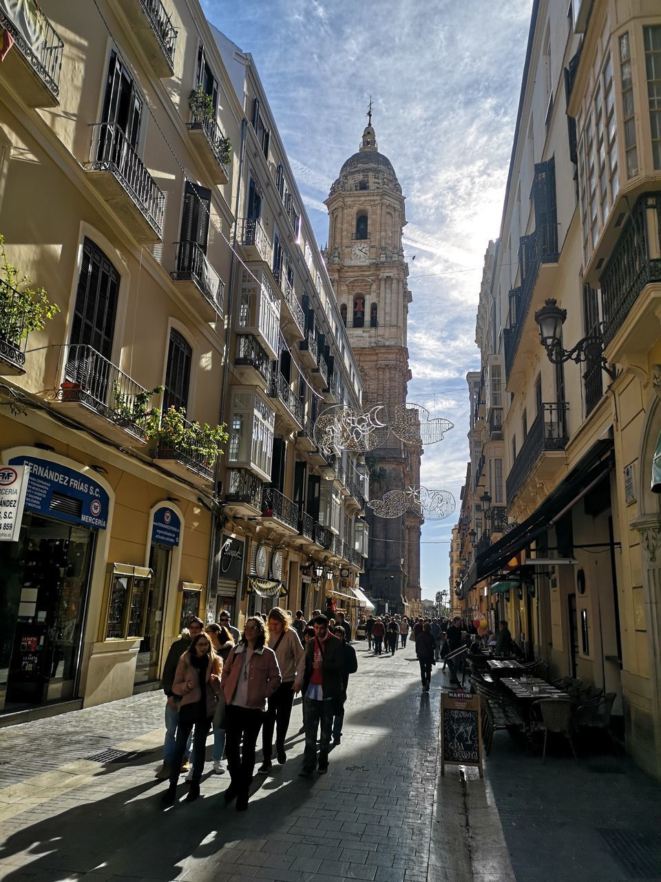 PEOPLE WALKING ON ROAD AMIDST BUILDINGS AGAINST SKY