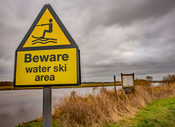 Information sign on road by field against sky