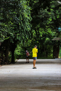 Rear view of 2 boys playing skateboard on footpath amidst trees