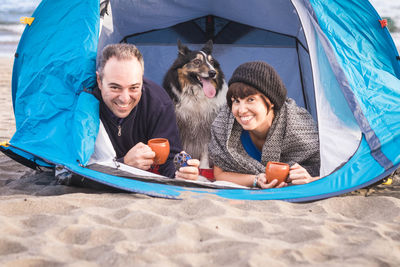 Portrait of cheerful couple with dog in tent at beach