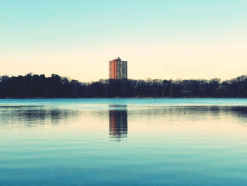 Scenic view of lake by building against sky at sunset