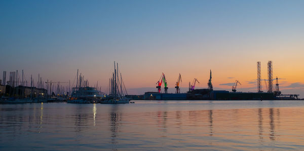 Sailboats moored in sea against clear sky during sunset