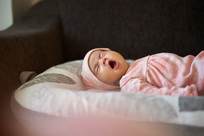 Newborn baby girl lying on her bed yawning 