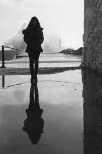 Full length of woman reflecting in puddle standing by wall