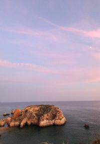 Rocks by sea against sky during sunset