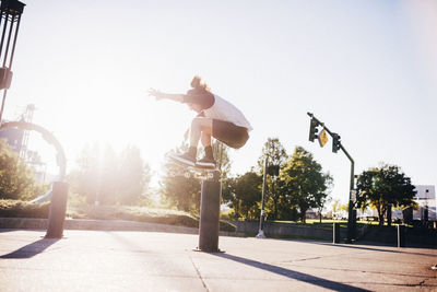 Man performing stunt with skateboard on city street against blue sky during sunny day