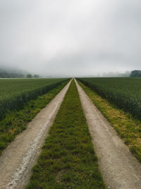 Empty road amidst field against sky