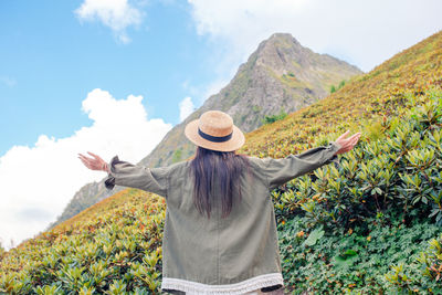 Rear view of woman with arms outstretched standing on mountain against sky