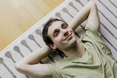 High angle view of carefree boy lying down with hands behind head on carpet at home