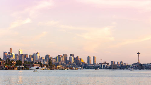Sea by buildings against sky during sunset