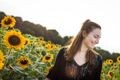 Portrait of young woman by sunflower on field against sky