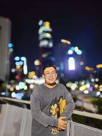 Portrait of man standing against illuminated city at night