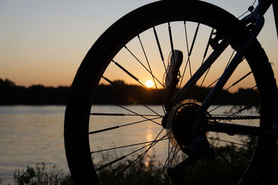 Close-up of bicycle wheel by lake against sky during sunset