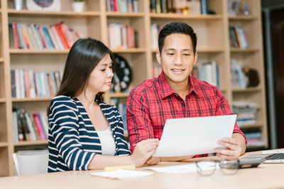 Friends studying while sitting at table in library