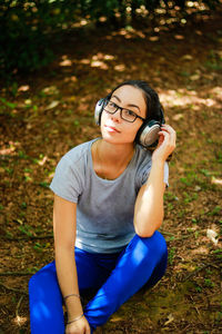 High angle portrait of young woman listening music while sitting on field in park