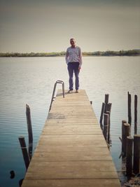 Man standing on pier over lake against sky