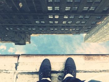 Low section of person standing by building reflection in puddle