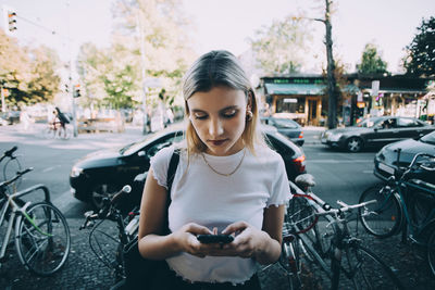 Young woman using mobile phone while standing on sidewalk in city