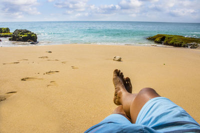 Low section of man relaxing on sand at beach