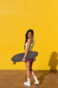 Full length portrait of woman standing against yellow wall