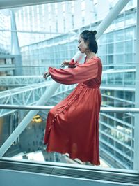 Young woman looking away while standing against window