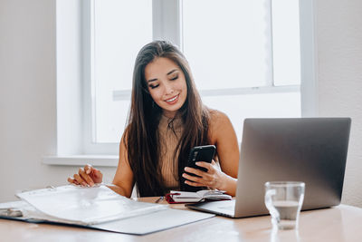 Young woman using phone while sitting on table