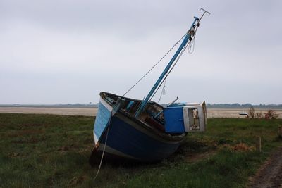 Abandoned boat on grassy field against sky