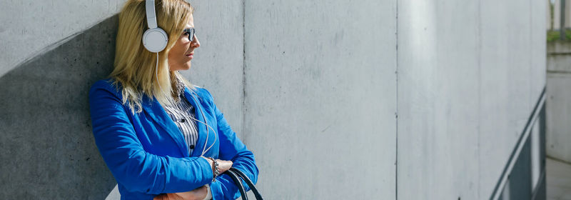 Panoramic view of businesswoman listening music on headphones while standing outdoors