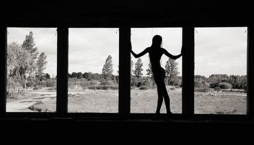 Silhouette man standing by window against sky