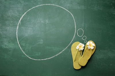 High angle view of blank speech bubble with flip-flops on blackboard