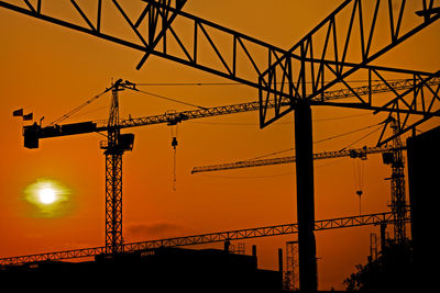 Silhouette cranes at construction site against sky during sunset