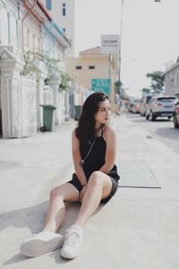 Young woman sitting on sidewalk in city