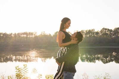 Side view of woman standing by lake against sky