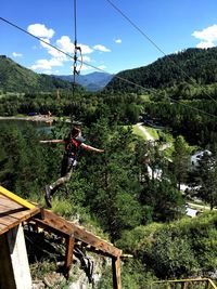 Woman zip lining over mountains against sky