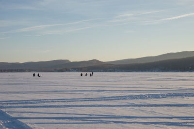 Fishermen sit and fish on the snow-covered lake in the evening light.