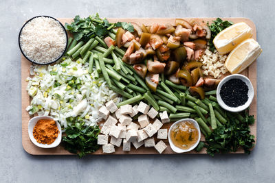 Top view of raw cut tomatoes with green beans and green onion with cheese and lemon and seasonings with rice in bowls on wooden board on table