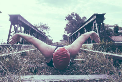 Woman lying down on railing against sky