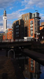 Bridge over canal by buildings against sky in city