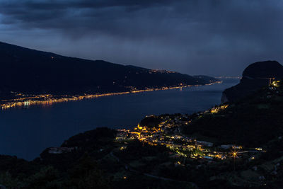 Illuminated city by sea against sky at night