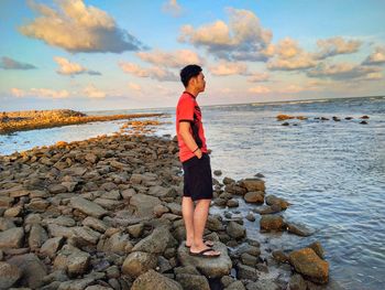 Full length of boy standing on rock at beach against sky