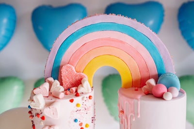 Big birthday cake with rainbow, colorful sprinkles. on many colorful heart balloons background.