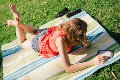 High angle view of woman reading in digital tablet while lying at park